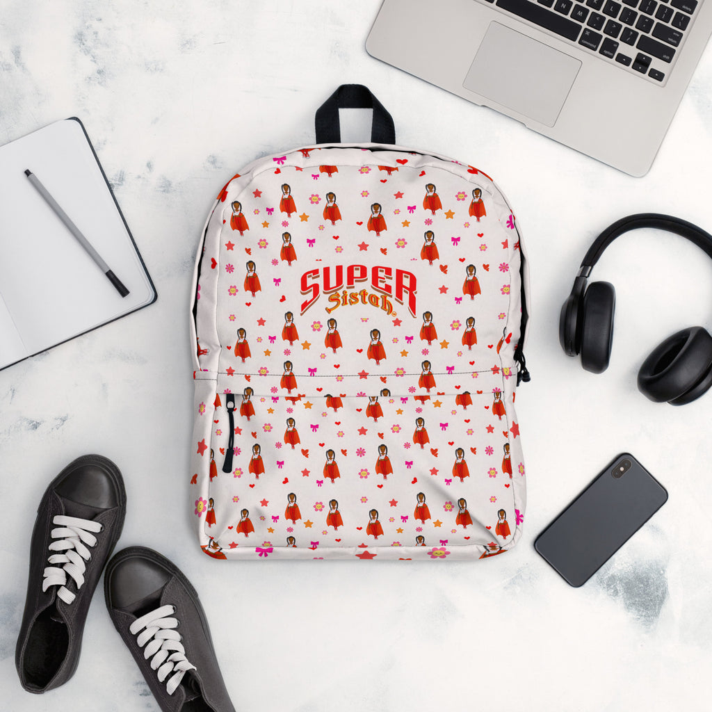 A white backpack with a repeating pattern of cartoon girls in red dresses and the words 'SUPER Sisters' in red and gold, styled in a flat lay with a laptop, headphones, shoes, and a phone on a marble surface.